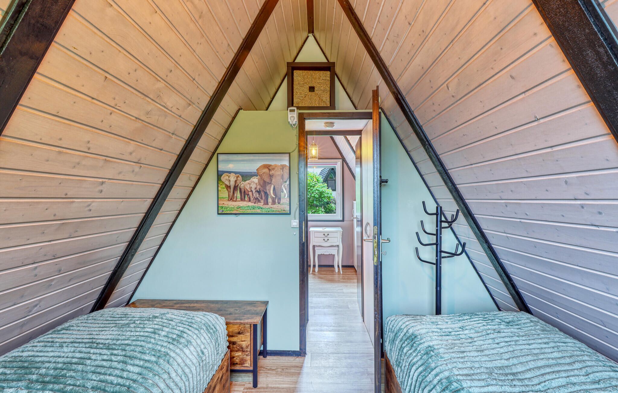 Een kamer in driehoekige vorm met houten wanden, twee bedden, een tafeltje, een schilderij van olifanten en een deur naar een balkon.