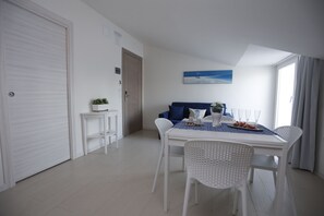 A modern room with a dining table, white chairs, a sofa, a small side table, and a painting on the wall. - Path House - Seaview Luxury by Wonderful Italy (Riposto)
