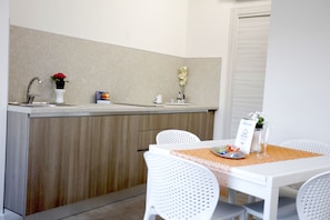 A kitchen with a sink, white chairs, a table with a placemat, and a sign. - Path House - Standard Etna 2 by Wonderful Italy (Riposto)
