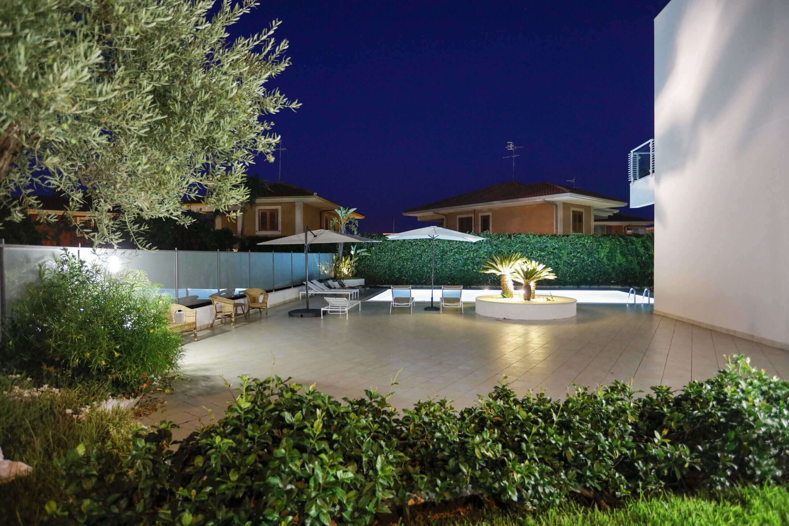 Ein Terrassenbereich im Freien mit Sitzgelegenheiten, einem kleinen runden Tisch und einem gut beleuchteten Pflanzenarrangement.