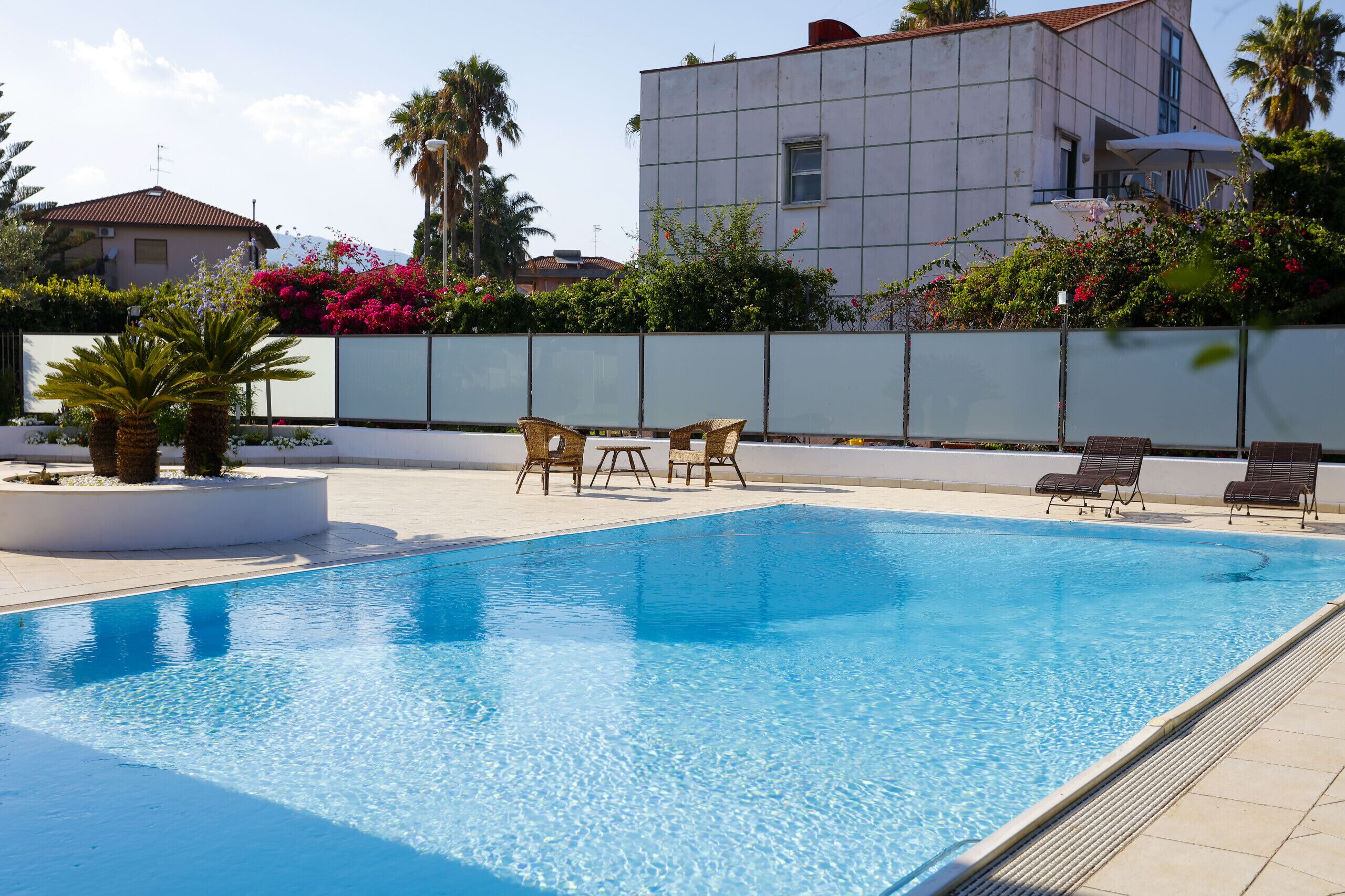 Une piscine avec des chaises longues, un mur blanc et un bâtiment en arrière-plan.