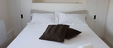 A neatly made bed with white and brown pillows, a white blanket, and two rolled white towels.