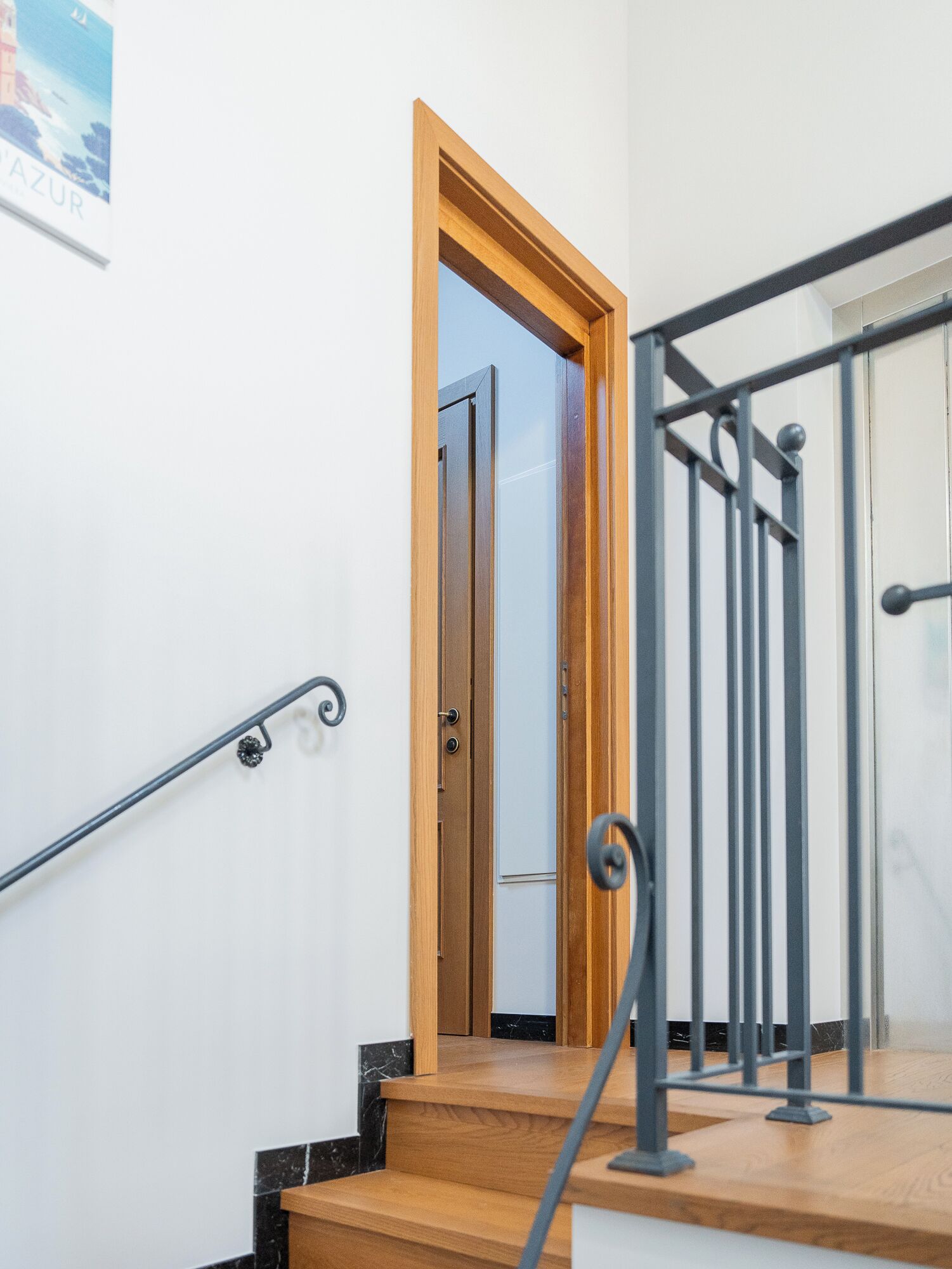 Un escalier en bois avec une rampe en métal, une porte donnant sur une autre pièce et une affiche accrochée au mur.