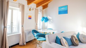 A room with a white sofa, blue chair, wooden floor, white walls, and a window with curtains. - Côte d'Azur Penthouse | 45 m² in Downtown Cannes (Cannes)