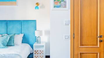 A bedroom with a bed, bedside table, lamp, wall art, and a wooden door.