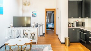 A modern room with a TV, white cabinet, dining table, and a view of a bedroom with a bed and curtains. - Côte d'Azur Penthouse | 45 m² in Downtown Cannes (Cannes)