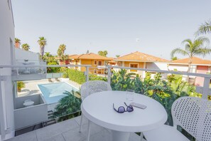 Een balkon met een ronde tafel, witte stoelen, een paar zonnebrillen en een smartphone op de tafel.