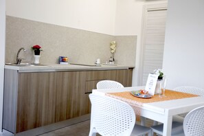 A kitchen with a sink, white chairs, a table with a placemat, and a sign. - Path House - Standard Etna by Wonderful Italy (Riposto)