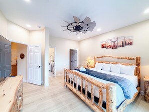 A bedroom with a wooden bed, a ceiling fan, and a door leading to another room. - 4BR Luxury Cabin | Hot Tub, Views & 3 King Master Suites (Bryson City)