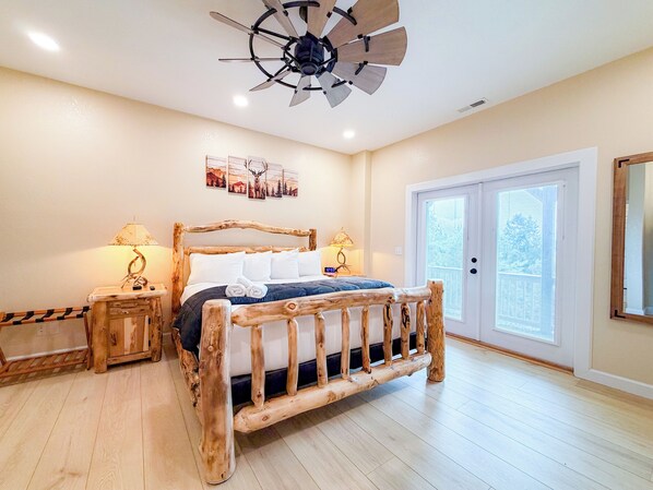 Une chambre à coucher avec un lit en bois, deux tables de chevet avec des lampes, un ventilateur de plafond et une grande fenêtre avec des stores.