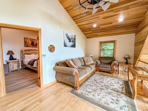 A spacious room with a wooden ceiling, a large sofa, a small table, and a bed with a headboard. - 4BR Luxury Cabin | Hot Tub, Views & 3 King Master Suites (Bryson City)