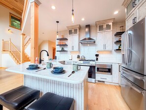 A modern kitchen with a central island, stainless steel appliances, and a wooden staircase. - 4BR Luxury Cabin | Hot Tub, Views & 3 King Master Suites (Bryson City)