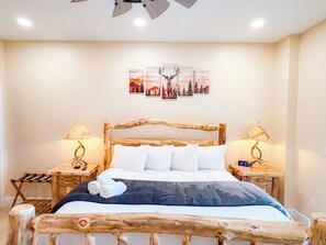 A bedroom with a wooden bed frame, white bedding, two bedside tables with lamps, and a wall-mounted artwork. - 4BR Luxury Cabin | Hot Tub, Views & 3 King Master Suites (Bryson City)