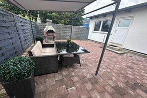 Eine Außenpatio mit Glastisch, Korbstühlen, Grill und Blumentöpfen.