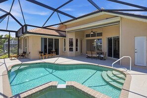 Una piscina con cerramiento de vidrio, un porche cubierto y mobiliario exterior.