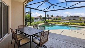 Un espace extérieur abrité comprenant une piscine, une table avec des chaises et une vue sur un quartier résidentiel.