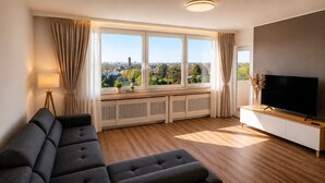 A modern living room with a sectional sofa, a flat-screen TV, and large windows offering a city view.