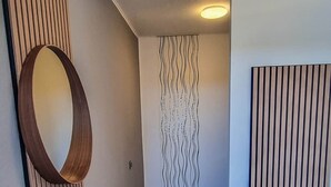 A hallway with wooden flooring, a circular mirror, a wall with a wavy pattern, and a bench.