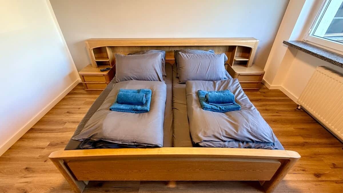 A twin bed with a wooden headboard, two bedside tables, and a window with a view.