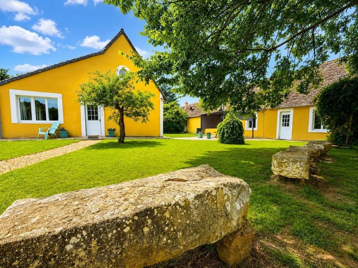 A yellow building with a white door and windows, surrounded by a well-maintained lawn and stone benches.