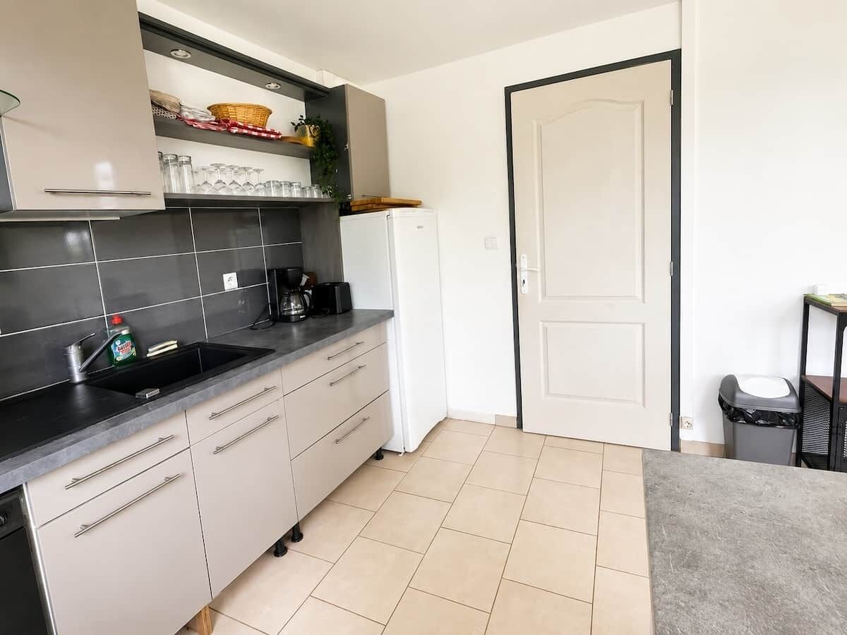 A kitchen with a sink, cabinets, a refrigerator, and a trash bin.