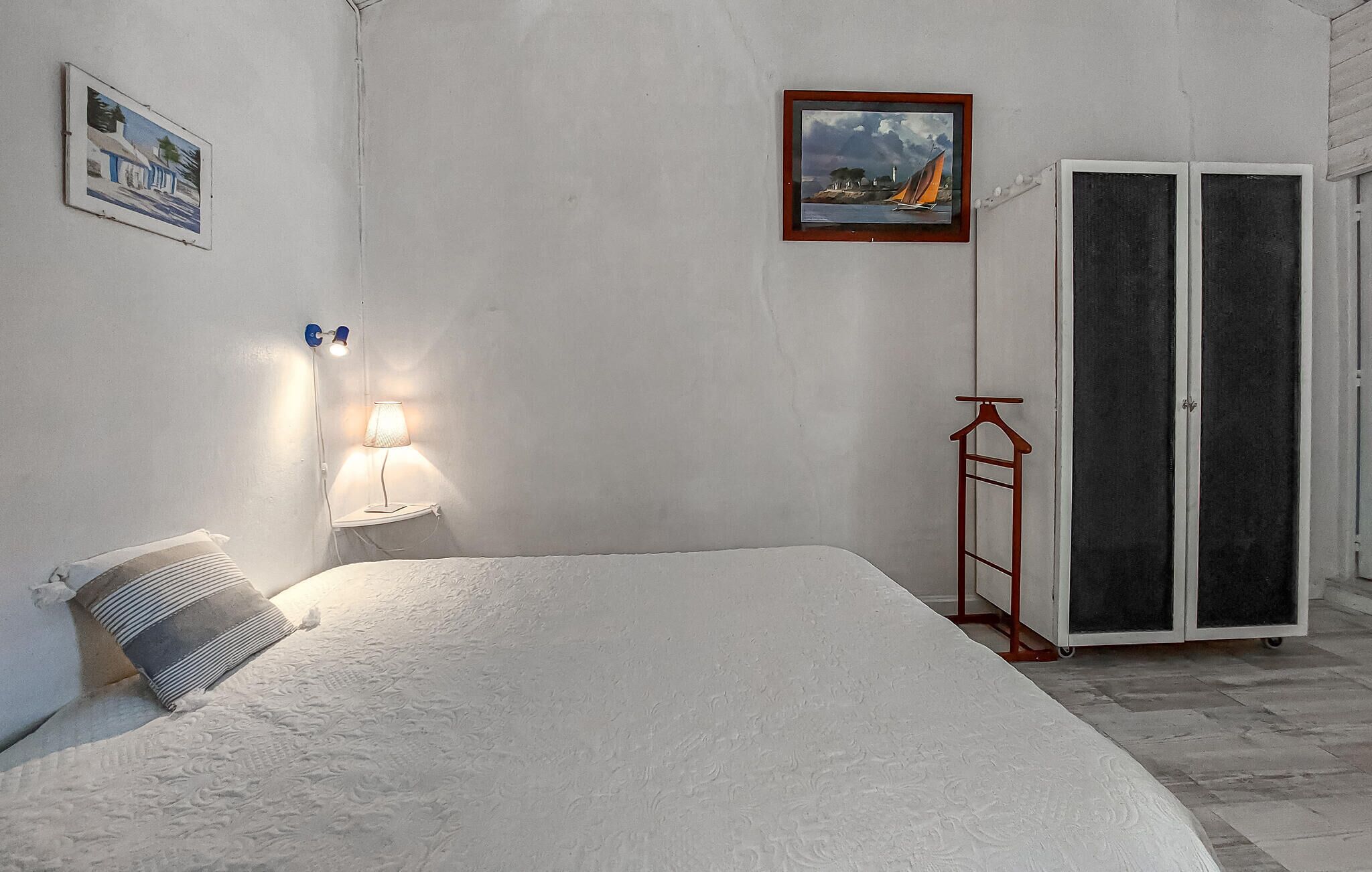 Une chambre à coucher avec un lit, une table de chevet avec une lampe, un tableau encadré au mur et une armoire.