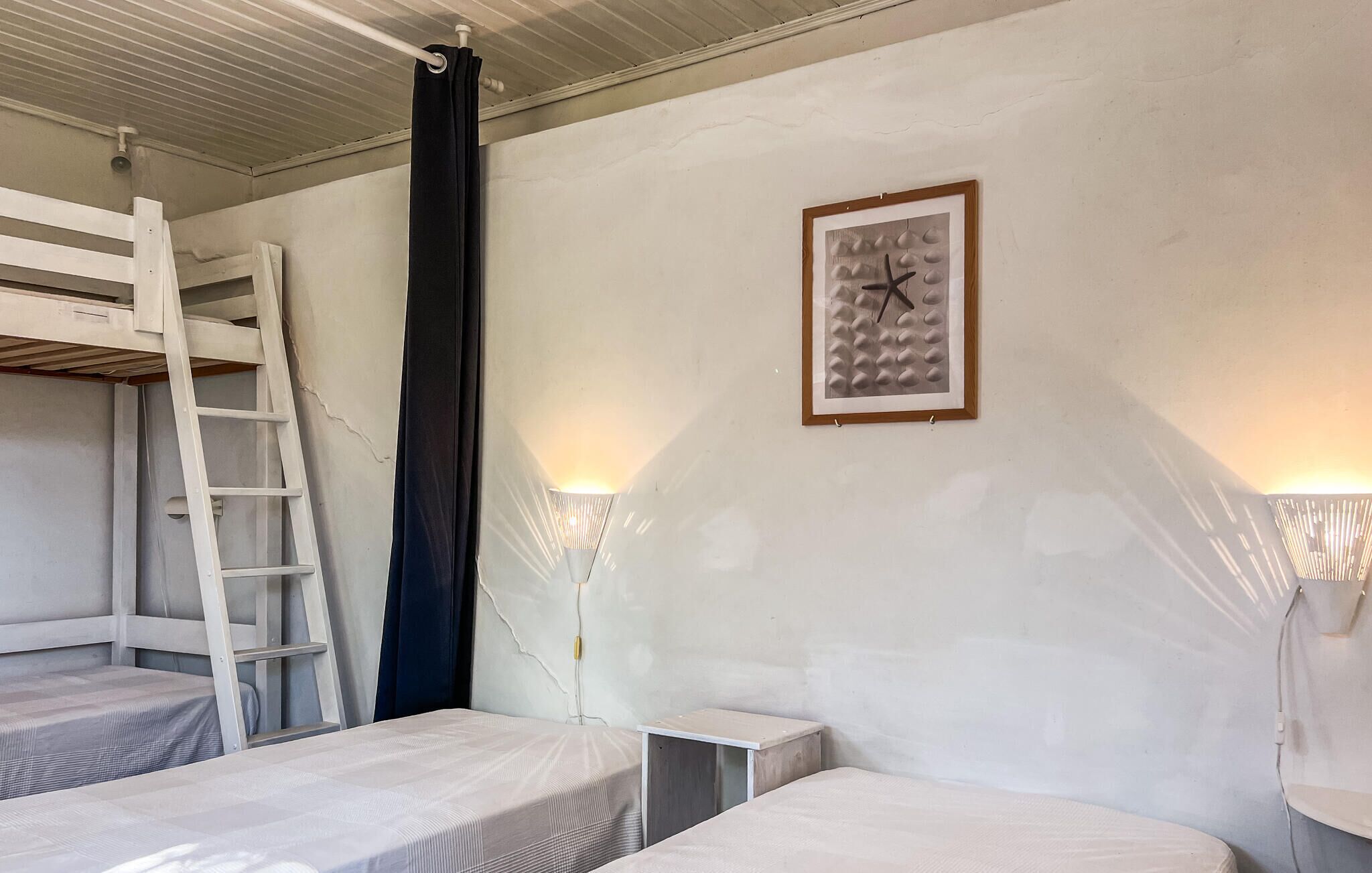 Une pièce avec des lits superposés, une échelle, un rideau noir, un tableau encadré et des lampes fixées au mur.