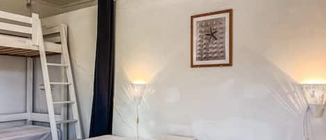 Une pièce avec des lits superposés, une échelle, un rideau noir, un tableau encadré et des lampes fixées au mur.