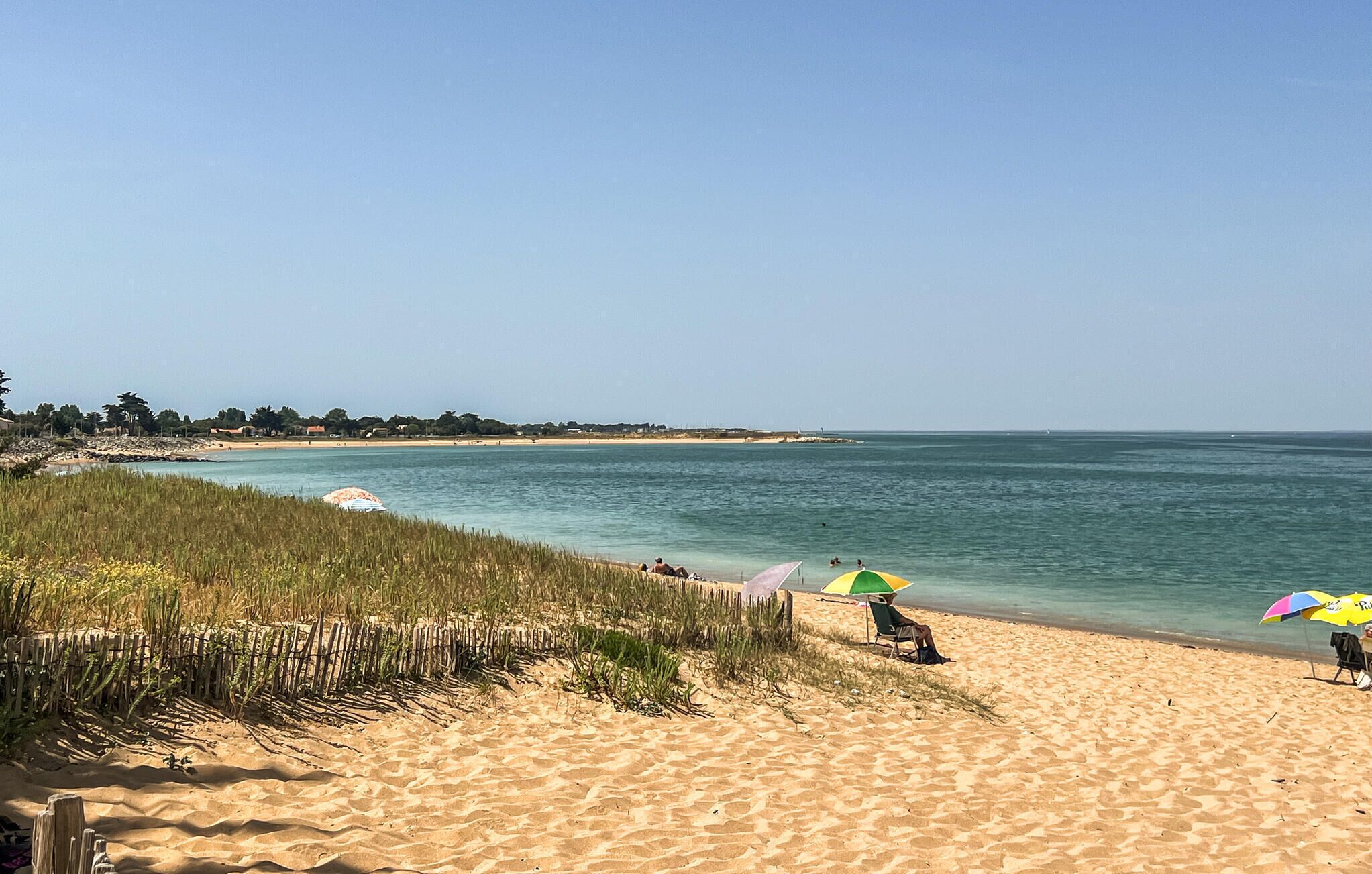 Uma praia com águas cristalinas, areal arenoso e alguns guarda-sóis.