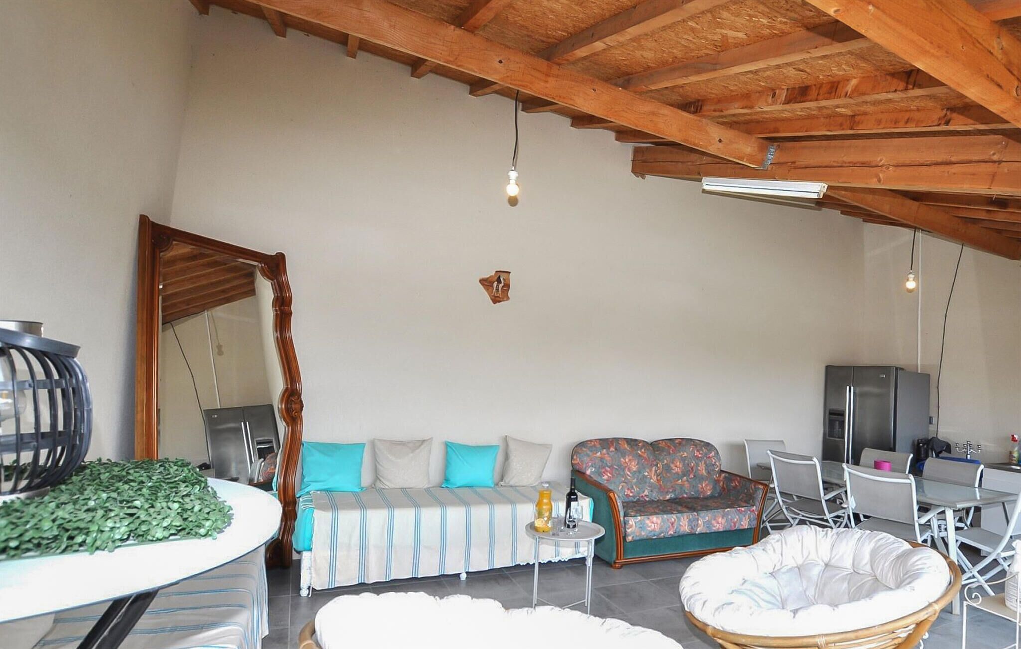 A spacious living area with a high ceiling, a sofa set, a dining table, and a wicker chair.