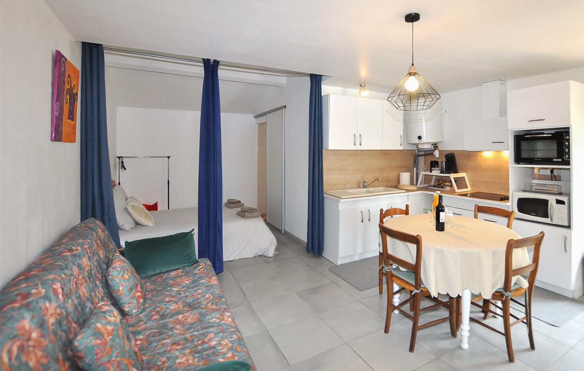 A compact living space with a sofa, dining table, chairs, kitchenette, and a bed with curtains.