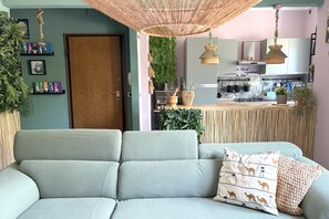 A living room with a sofa, a hanging light fixture, and a kitchen area in the background. - CV023 - Cervia, new three-room apartment with balcony and parking space (Cervia)