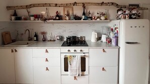 Een keuken met witte kastjes, een fornuis, een spoelbak en een koelkast.