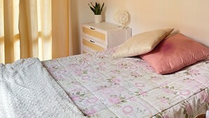 Een slaapkamer met een bed, nachtkastje met lamp, een plant en een schilderij aan de muur.