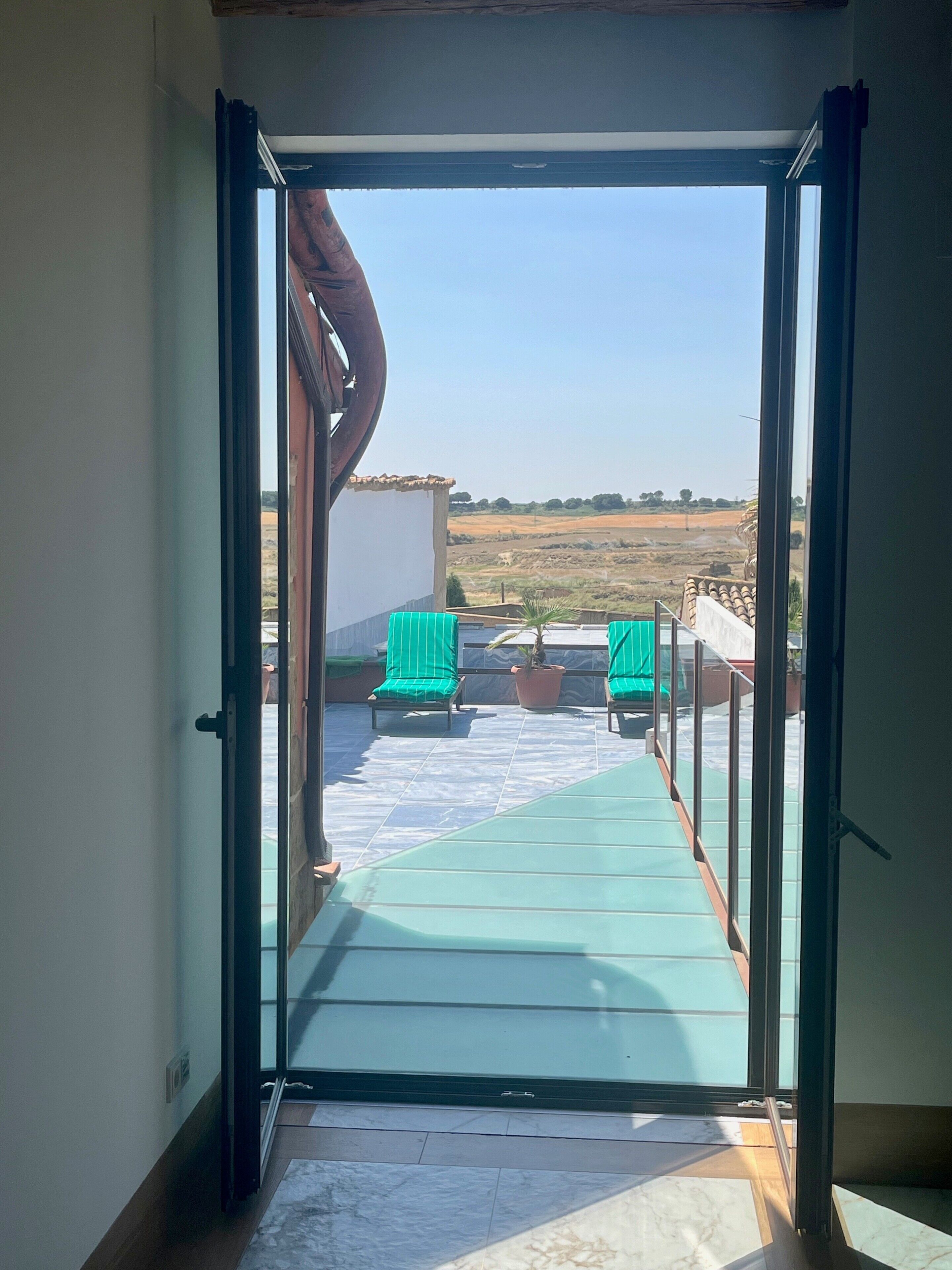 Een open deur die leidt naar een balkon met groene stoelen en een potplant.