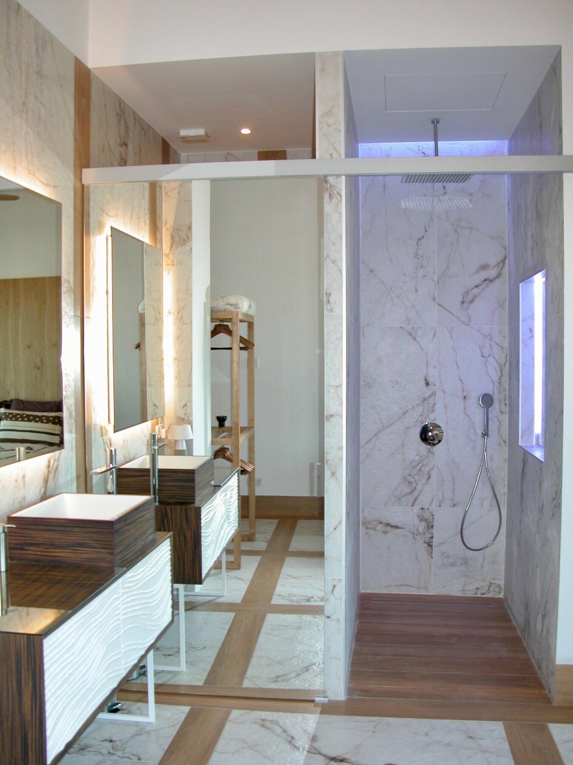 A modern bathroom with a large mirror, a vanity with a sink, a shower with a handheld showerhead, and a wooden floor.
