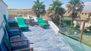 A rooftop terrace with lounge chairs, a small table, and a view of the surrounding landscape.