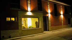 Un edificio con un ventanal grande y una puerta, iluminado por luces exteriores.