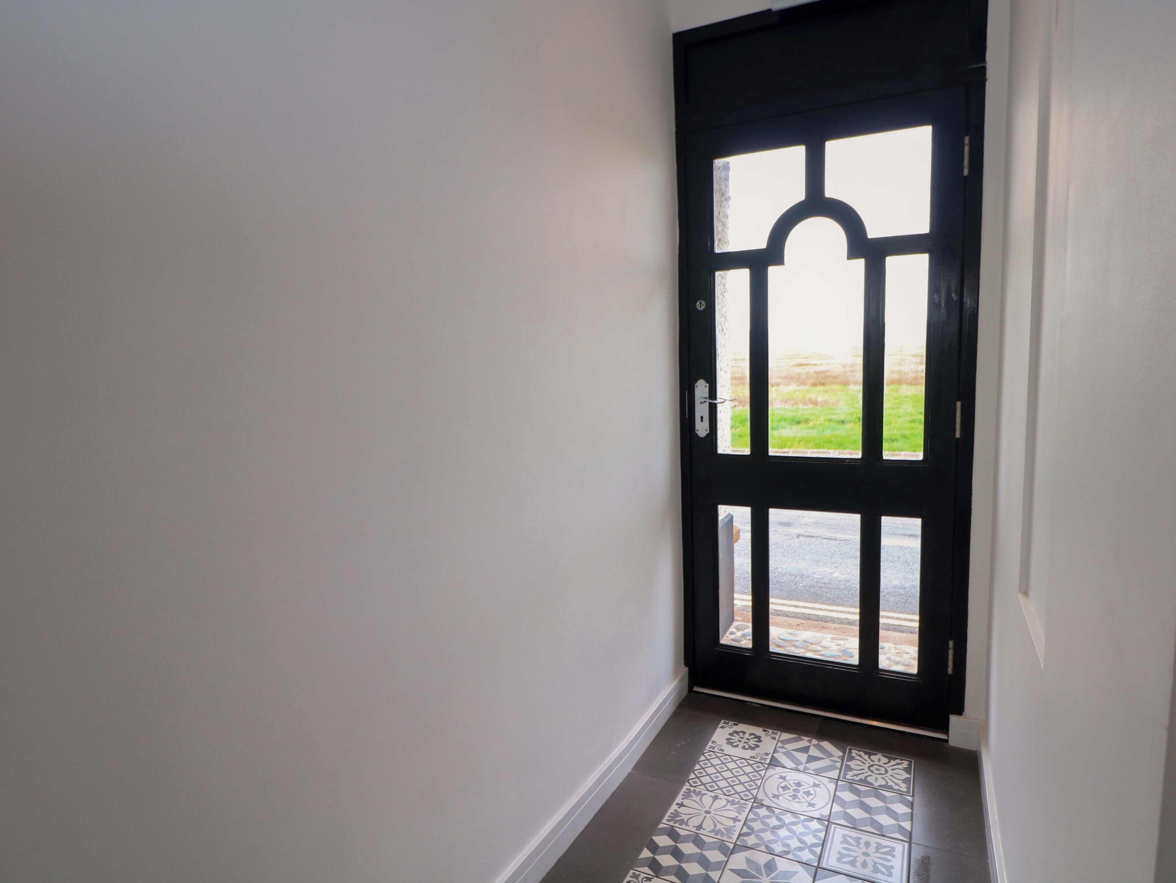 A black door with a geometric pattern on the floor leading to an outdoor area.