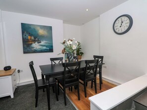 A dining area with a table, chairs, a clock, a painting, and a vase with flowers. - Broad Beams (Neston)