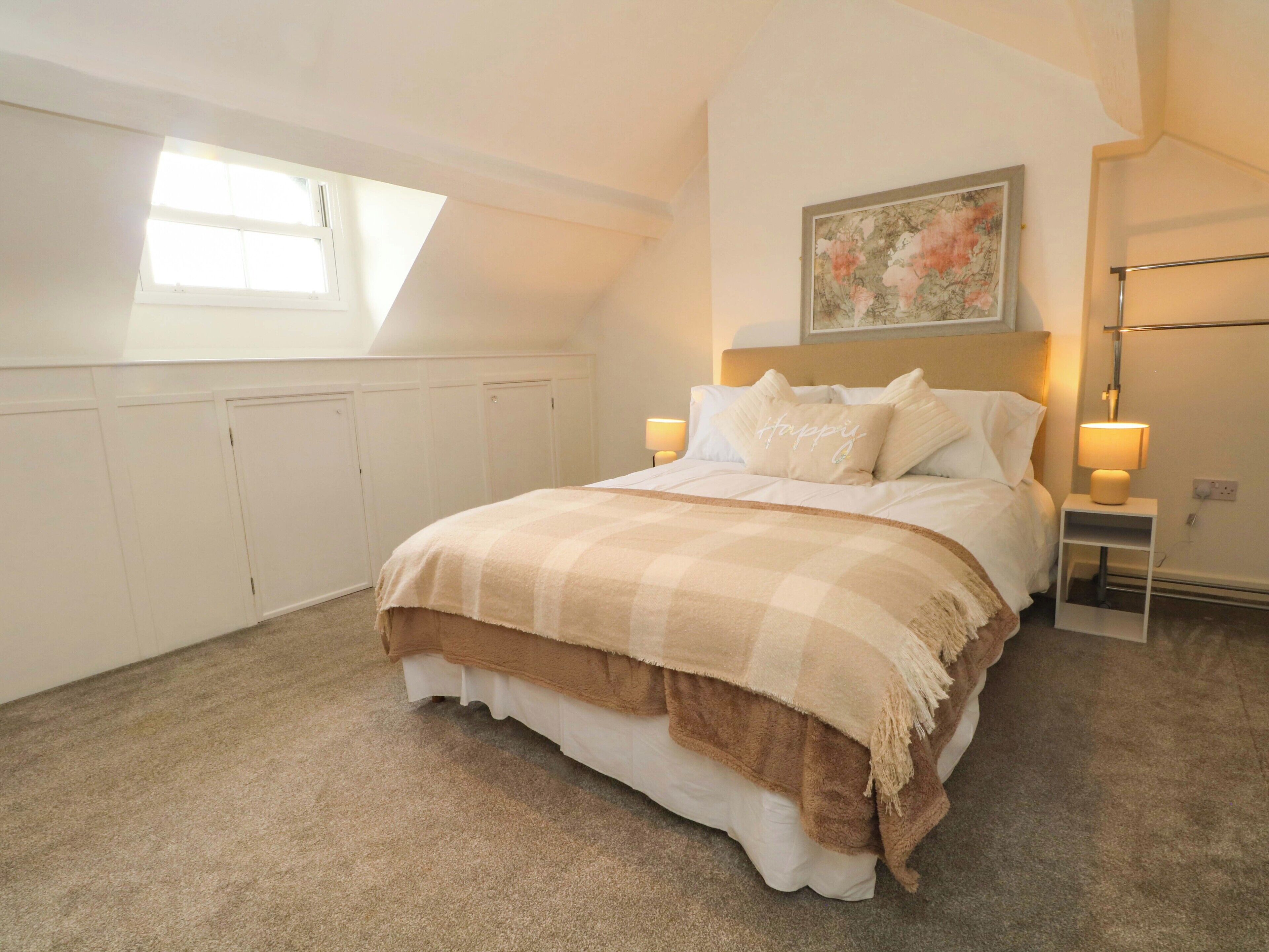 A bedroom with a bed, two bedside tables, a nightstand, a window, and a painting on the wall.