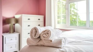 A neatly made bed with rolled towels, a white dresser with drawers, and a window with a view of greenery.
