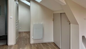 Een kamer met een schuine kap, dakraam, radiator en een deur naar een andere kamer.