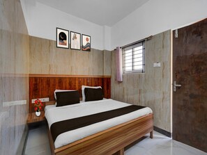 Ein Schlafzimmer mit Holz-Kopfteil, einem Bett mit weißer und schwarzer Bettwäsche, einem Nachttisch mit Blumenvase und einem Fenster mit Vorhang.