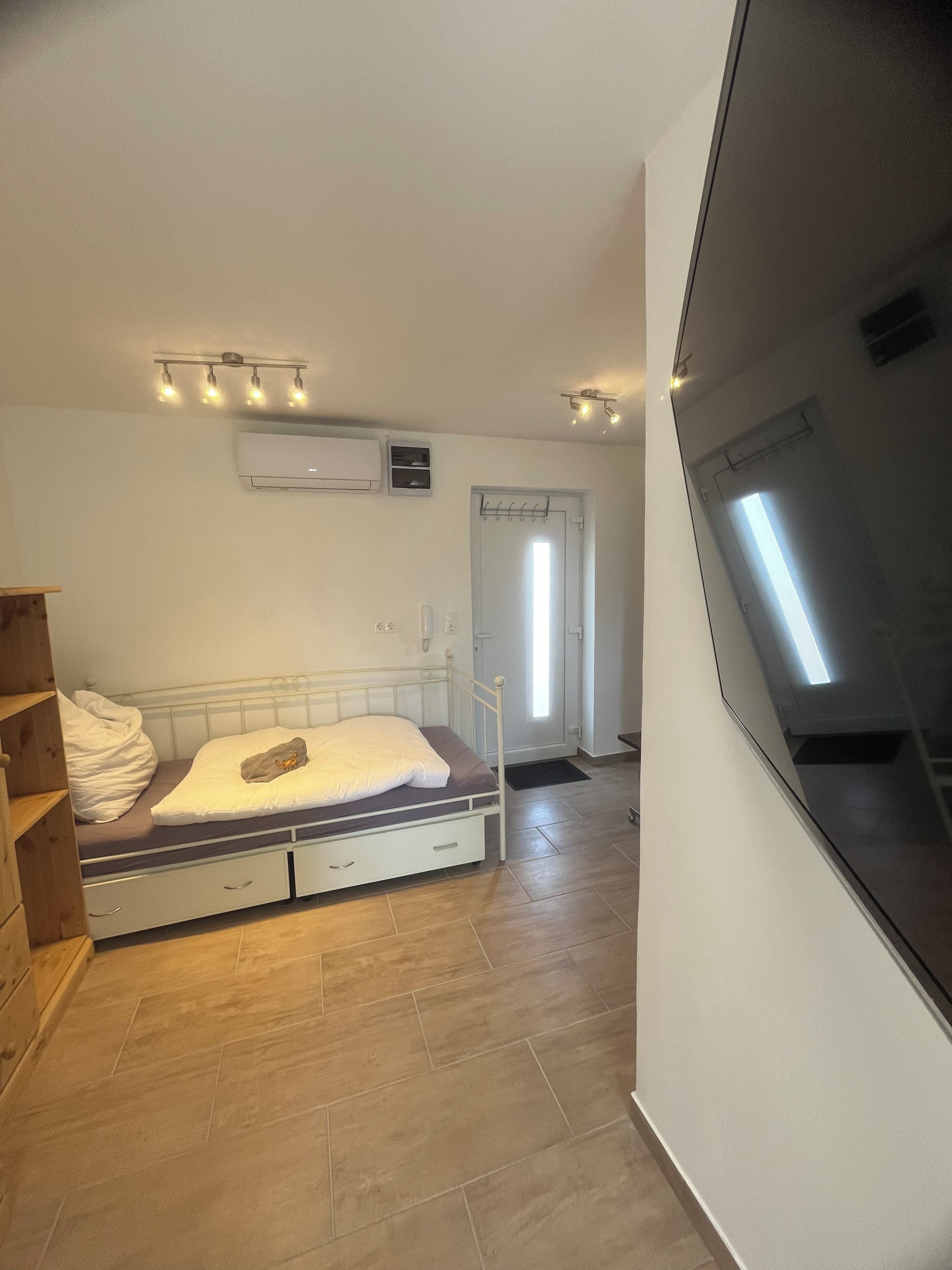 Une chambre à coucher comprenant un lit, une étagère en bois, un appareil de climatisation et une porte donnant sur une autre pièce.
