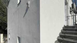A building with a grey exterior, a set of stairs, and a window with an air conditioning unit. - Beautiful vacation rental 200 meters from Lake Balaton for up to 4 people, with a balcony (Siófok)