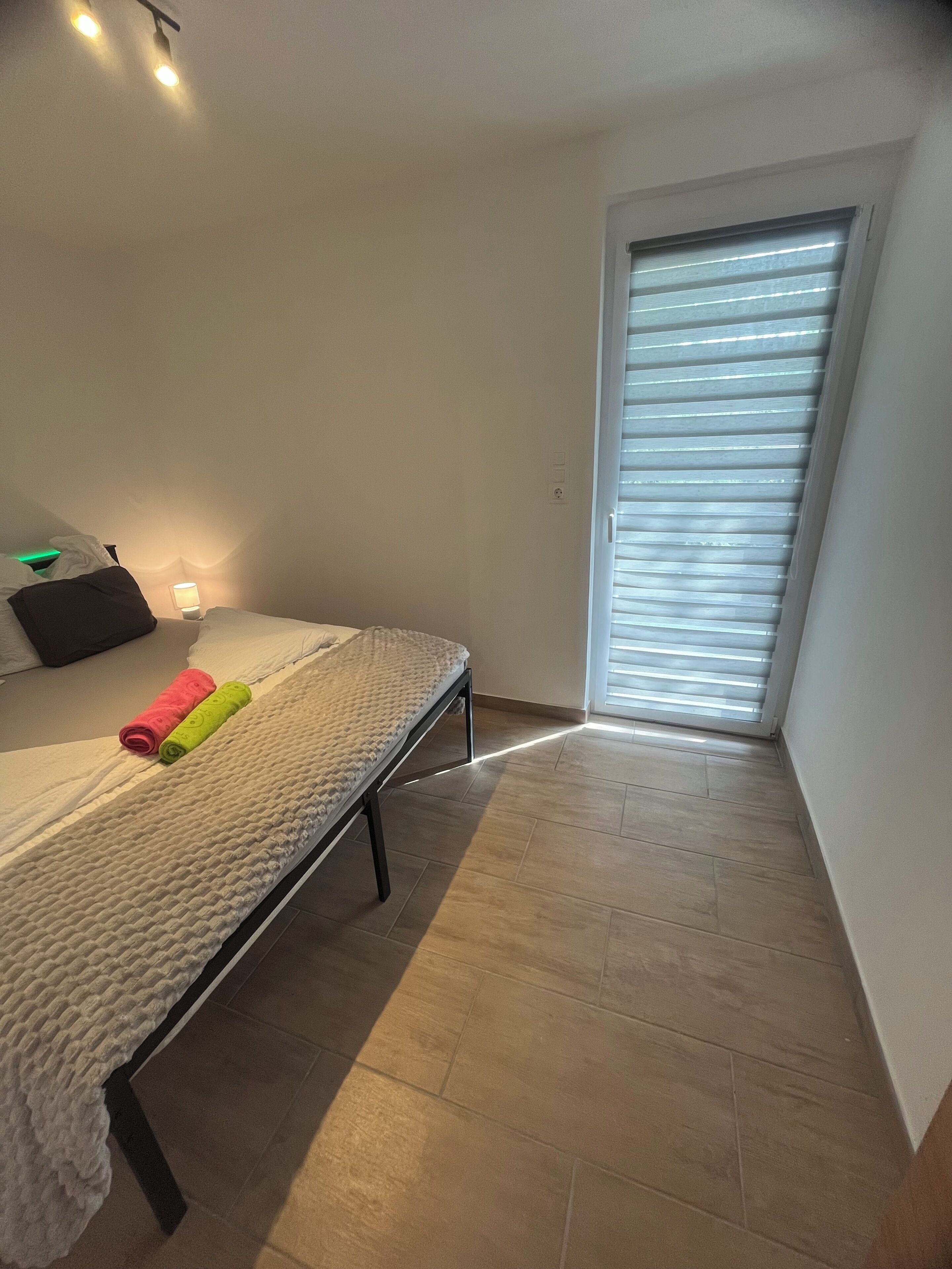 Une chambre à coucher avec un lit, une lampe de chevet, une fenêtre avec des stores et une petite table avec une lampe.