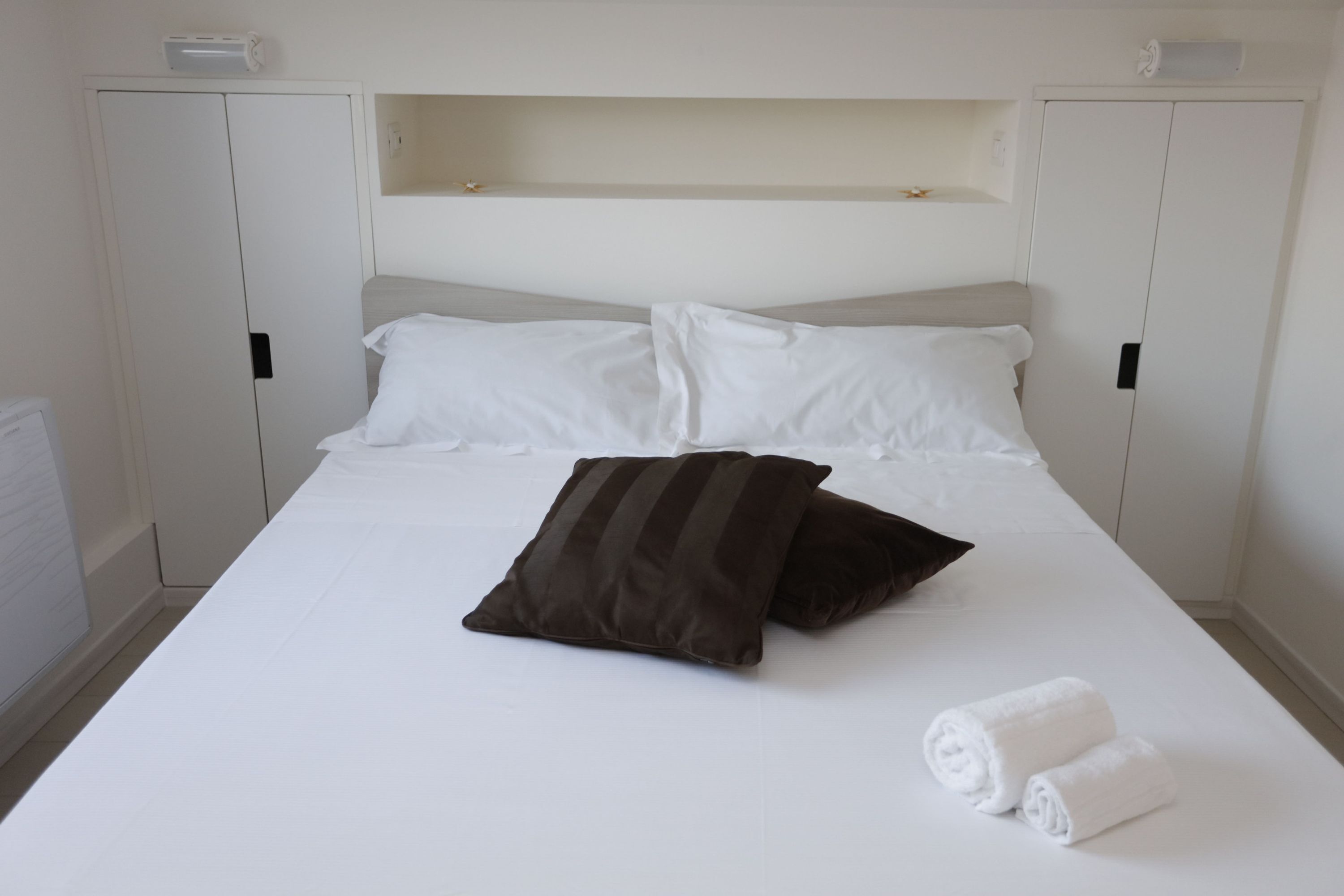 Ein Bett mit weißer Bettwäsche, zwei Kissen und zwei zusammengerollten Handtüchern.