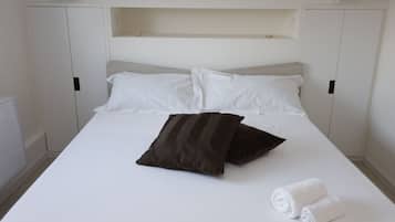 Ein Bett mit weißer Bettwäsche, zwei Kissen und zwei zusammengerollten Handtüchern.