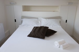 Una cama con sábanas blancas, dos almohadas y dos toallas enrolladas.